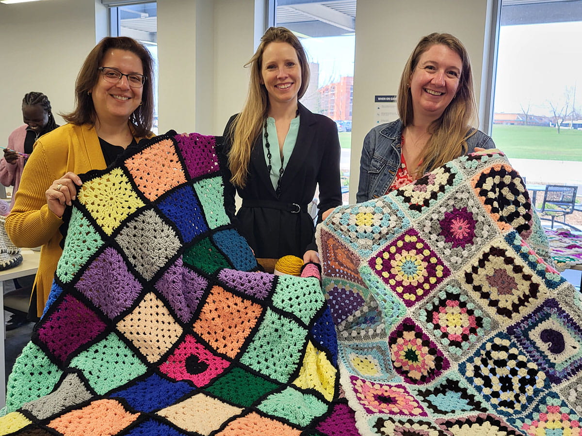 Three women holding two crocheted blankets